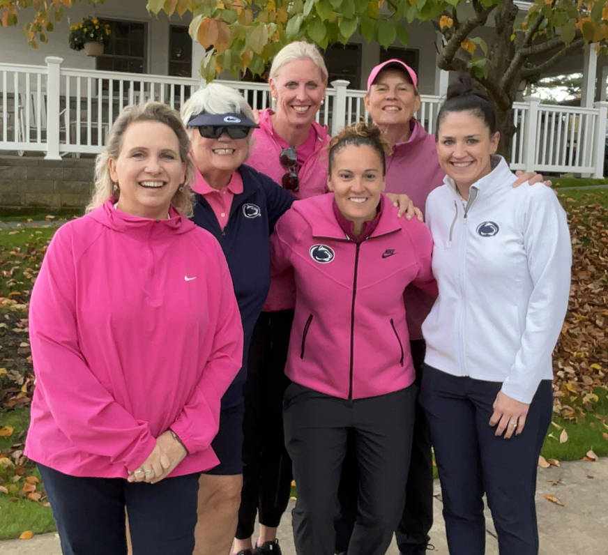 A group of smiling, pink clad golfers and organizers